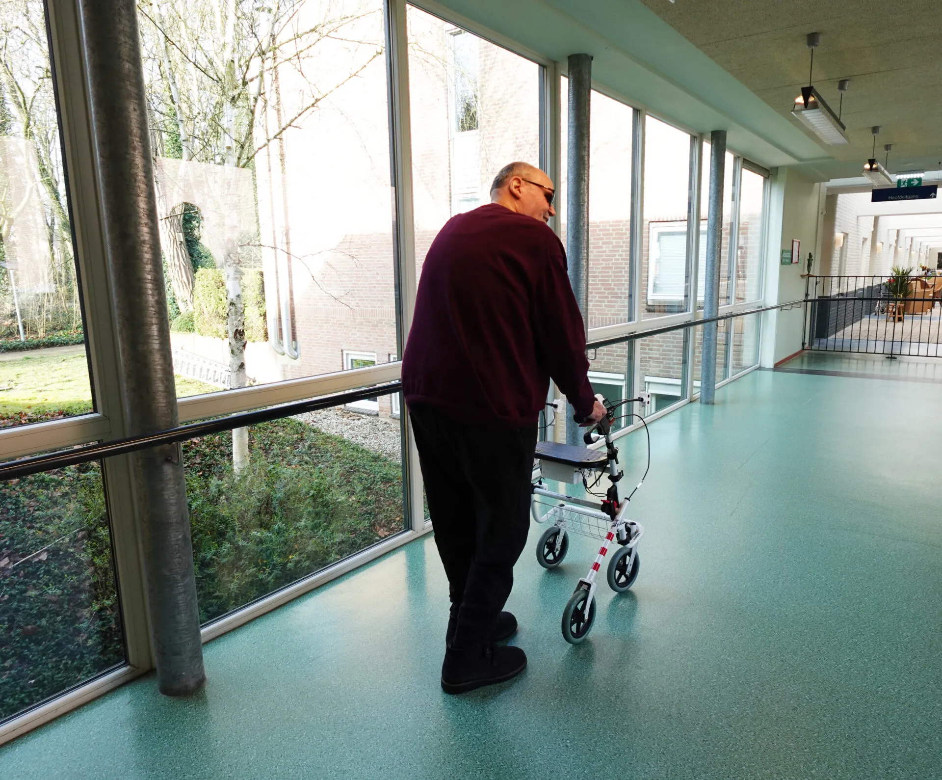 Bewoner Het Schild loopt in de gang met trillende rollator