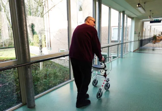 Bewoner Het Schild loopt in de gang met trillende rollator