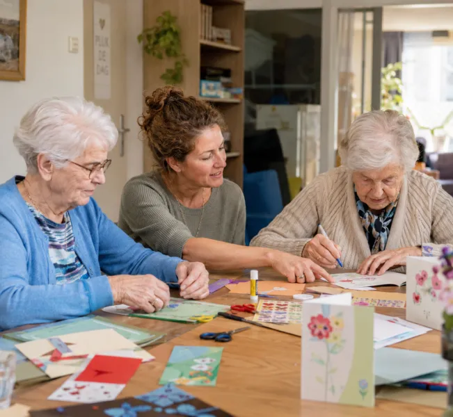 Vrijwilliger samen met clienten bij kaarten maken activiteit